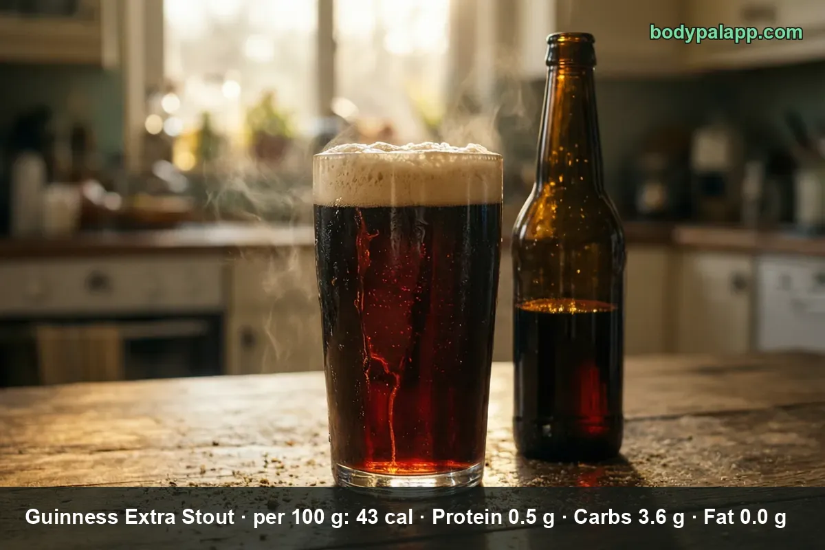 Pint of stout with a thick head, the beer glowing red-brown, beside an unlabeled brown bottle on a wooden table.